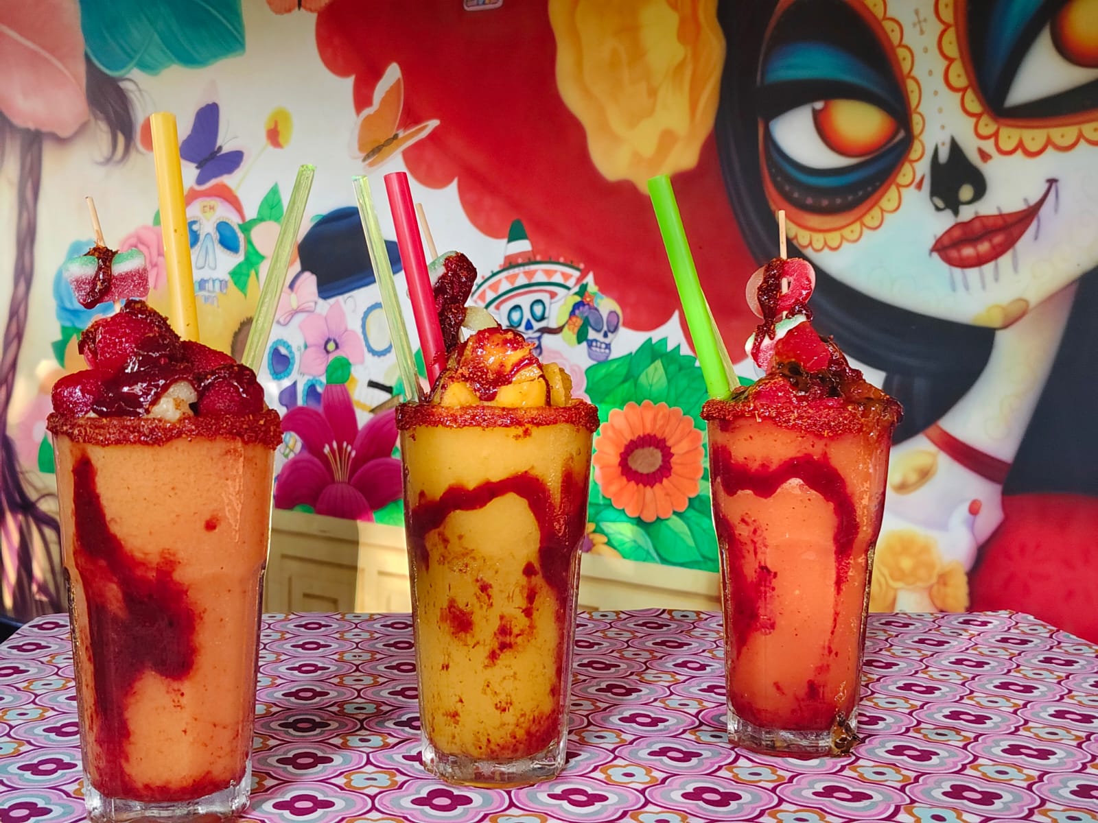 Tres chamoyadas de MirRey frente a un mural mexicano